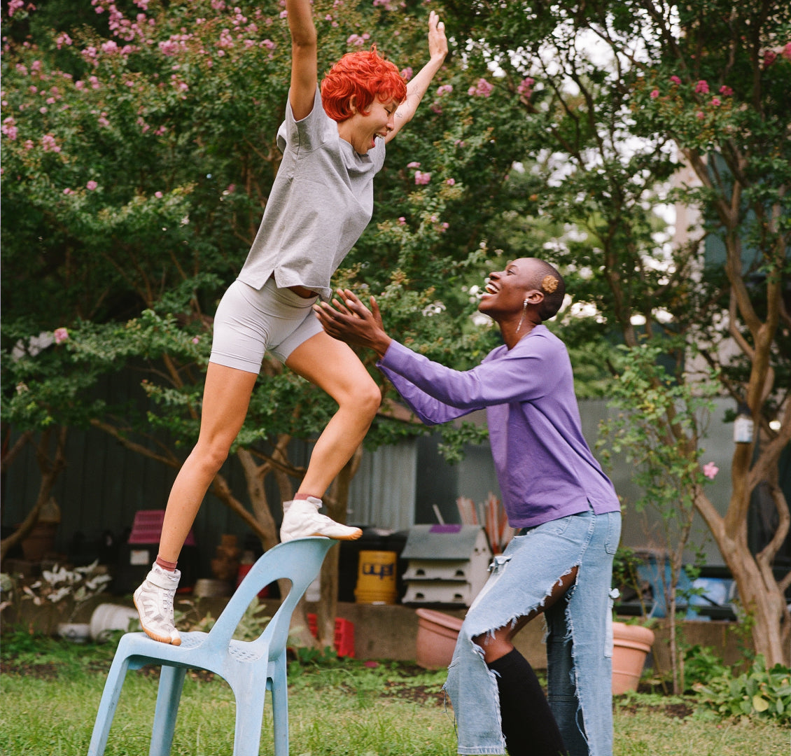 Person standing on chair with arms up, being caught by another person, both with joyful expressions