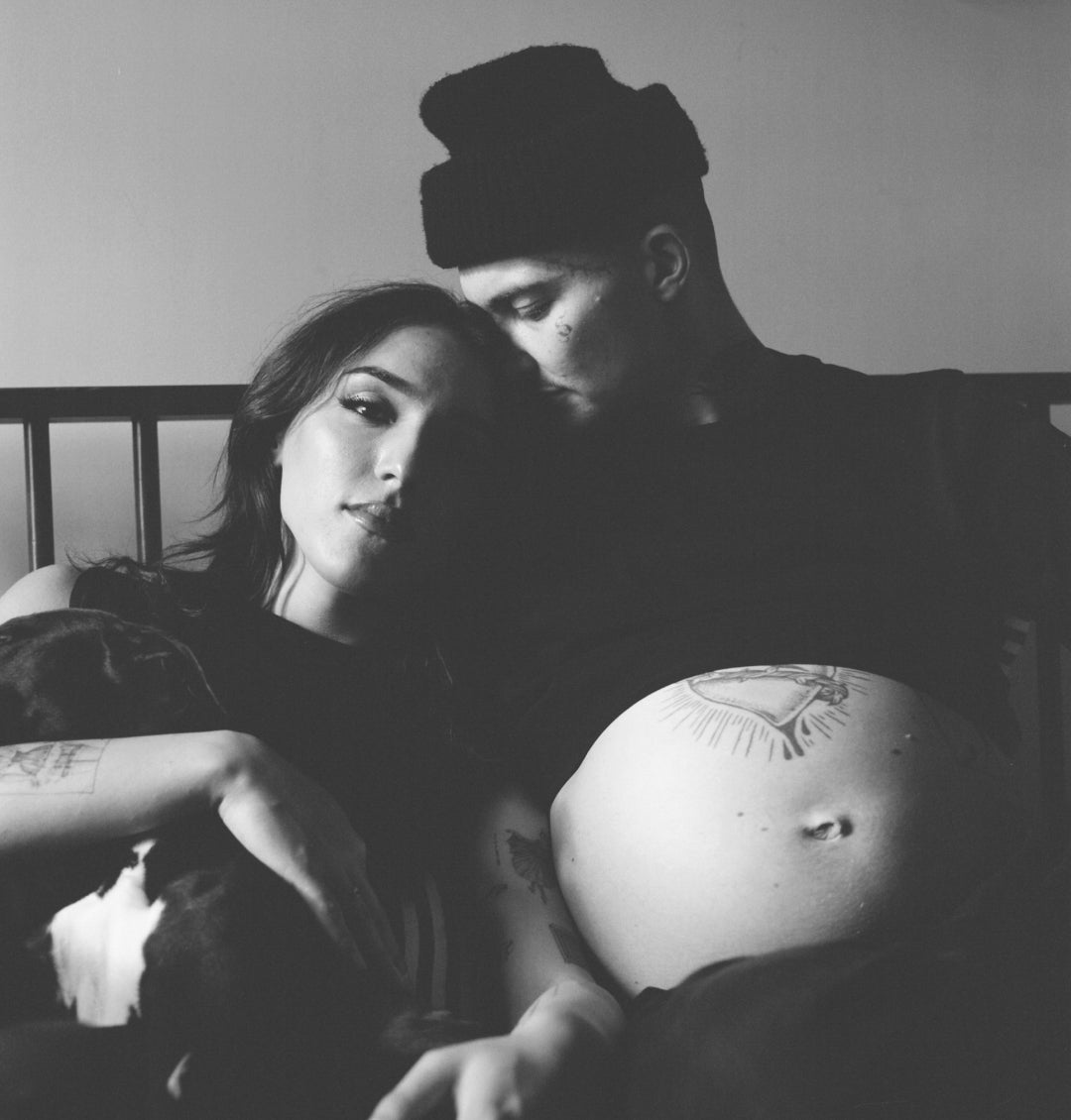 Arthur, pregnant, leaning against his partner Santana
